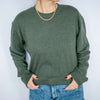 Person wearing a green Excel Therapy Services sweatshirt and blue jeans with a gold chain necklace against a white background